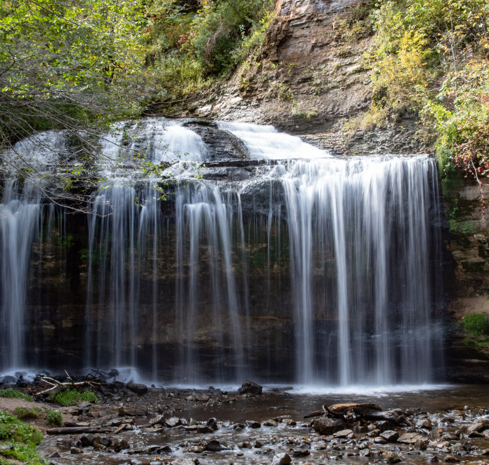 Small waterfall cascading over rocky ledge, surrounded by greenery.
