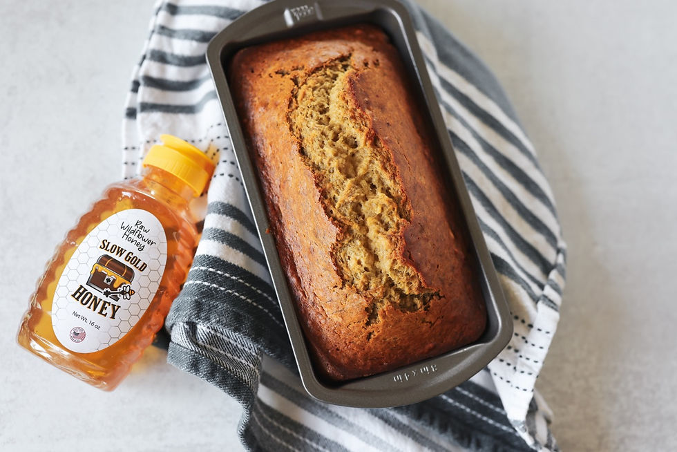 An overhead photo of finished honey banana bread in the loaf pan with a golden top. Sitting upon a striped dish towel, with a bottle of SlowGold Honey resting next to it.