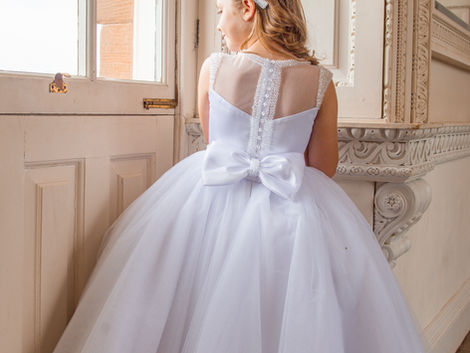 White communion dress from crystal and pearl boutique with mesh panelling, glass buttons and bow at the back