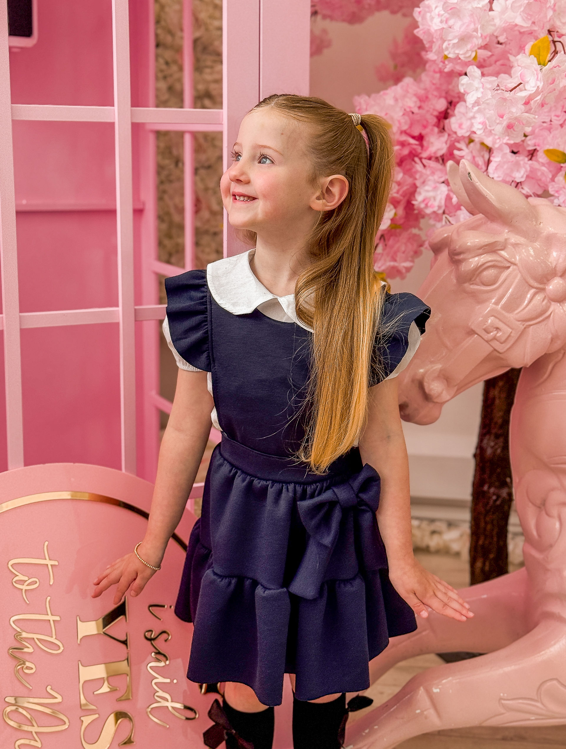girl wearing a navy school pinafore with a bow from crystal and pearl boutique