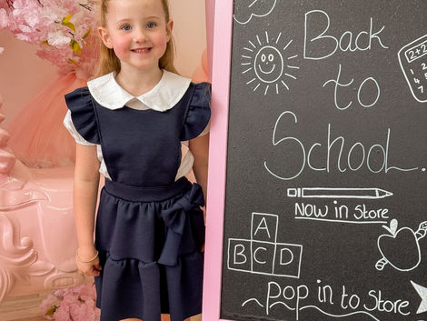 Girl wearing Crystal and Pearl Boutiques school wear collection with shirt and navy ruffle pinafore