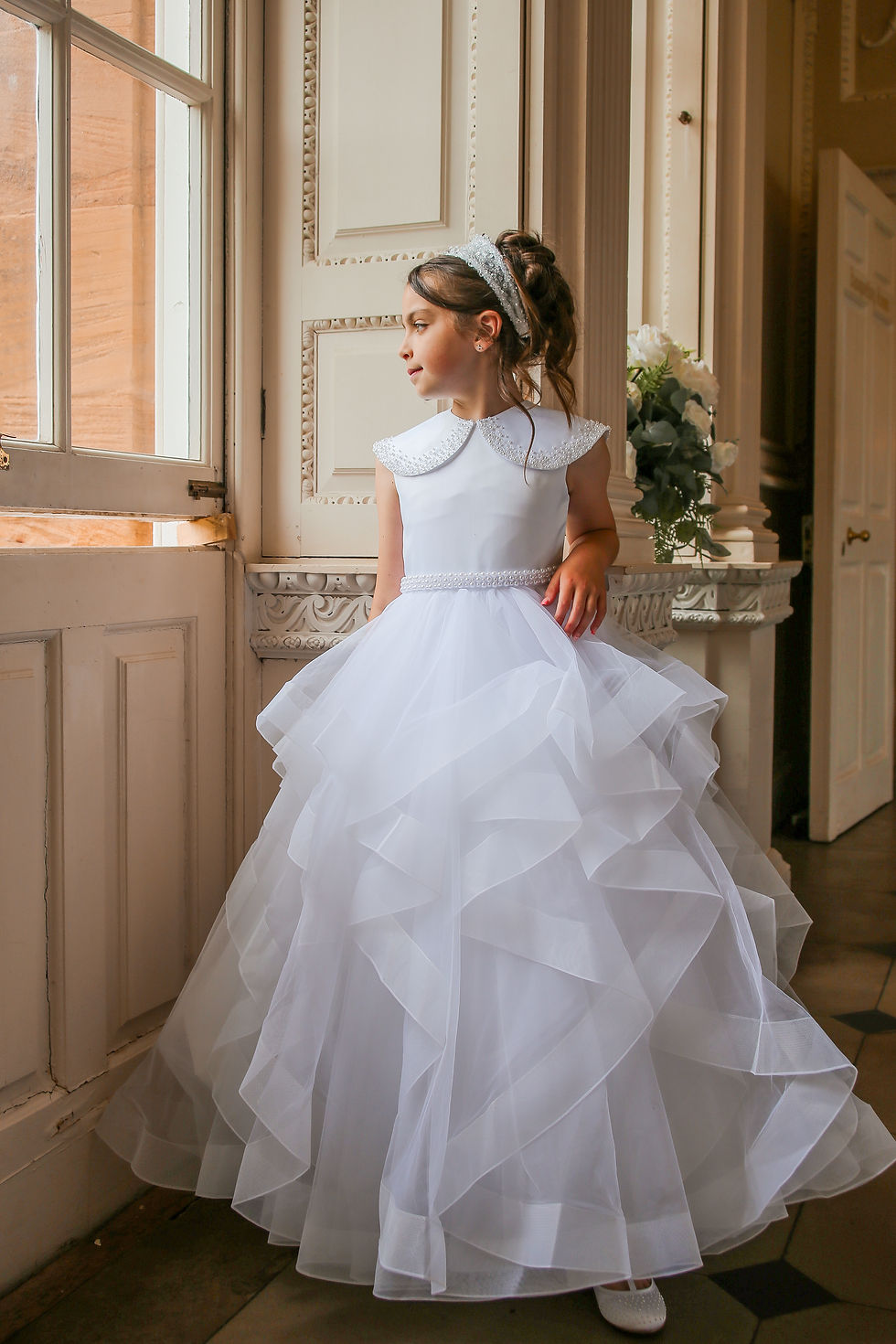 girl wearing white crystal and pearl boutique holy communion dress with ruffle skirt and embellished collar