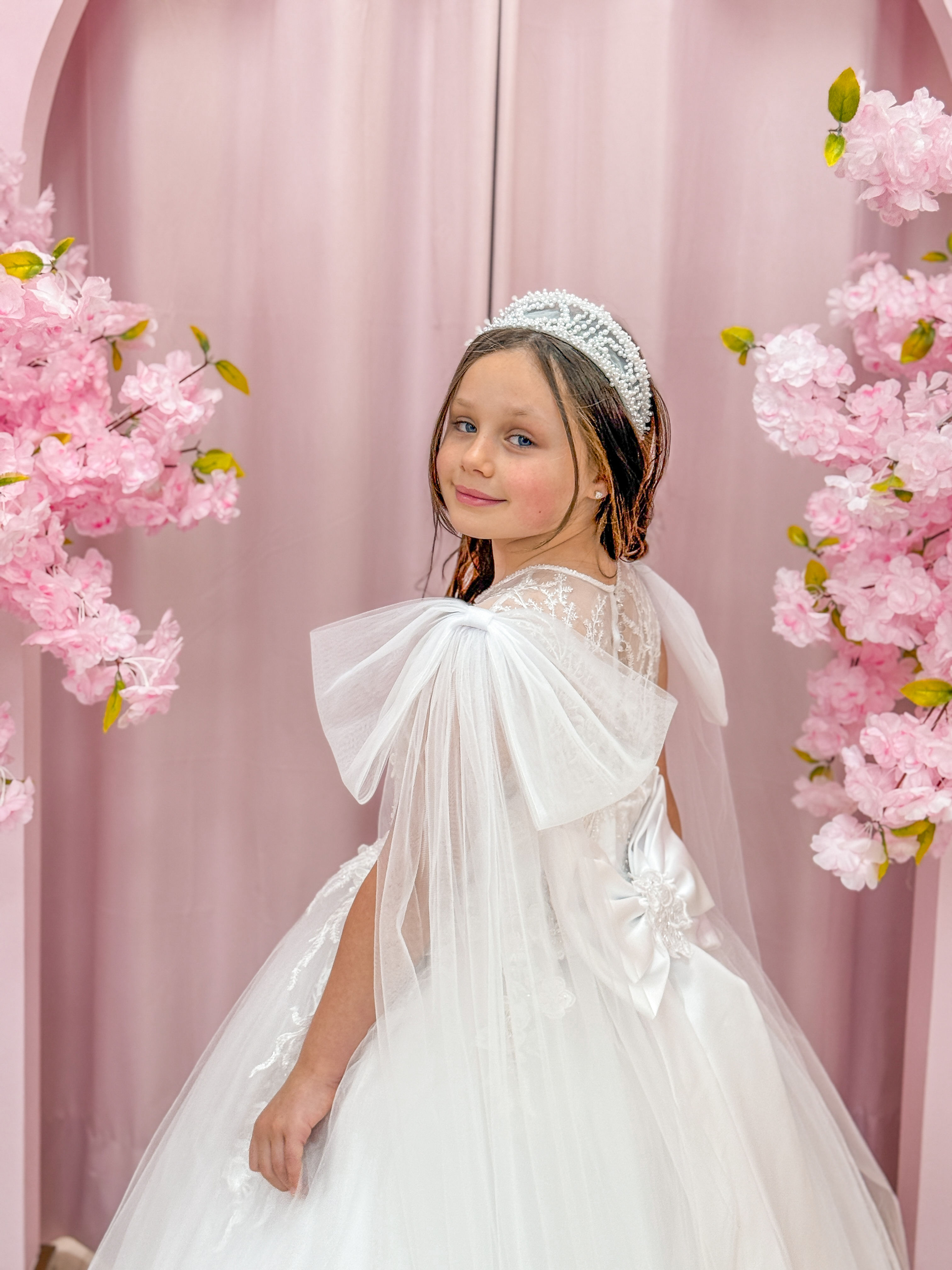 The Kris Dress – a handmade girls’ communion dress featuring delicate lace, soft tulle sleeves, and a satin bow. A timeless d
