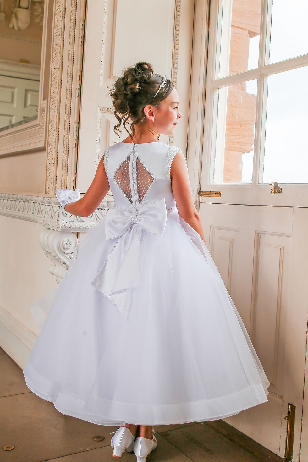 girl wearing c crystal and pearl boutique white satin holy communion dress with mesh embellished panel and bow at the back