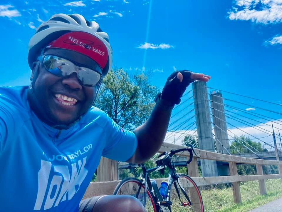 Cyrille on the Twin Cities Rail Trail posing close to the Arthur J. DiTommaso Memorial Bridge.