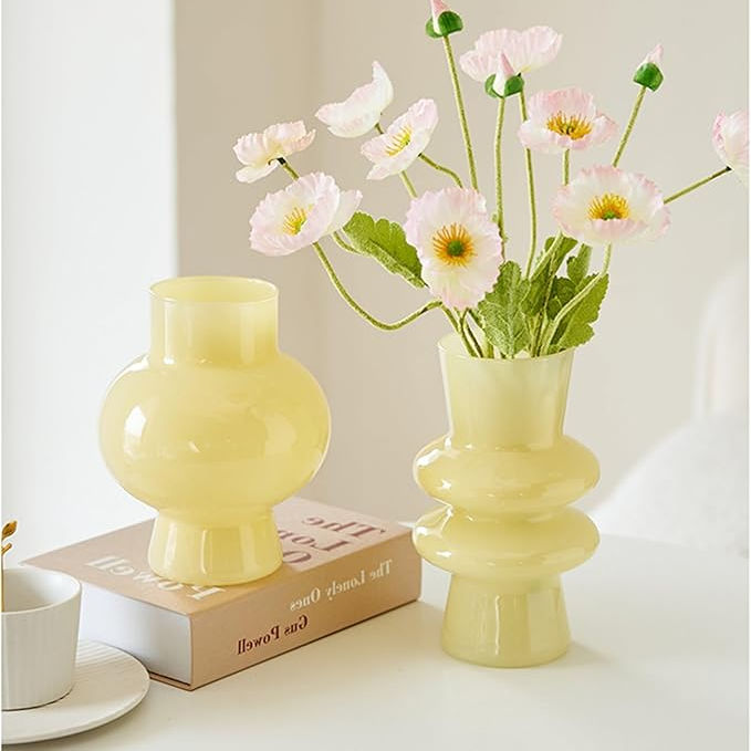Yellow vases with pink flowers on a book in a bright room. A white cup is on the side, creating a serene and decorative scene.