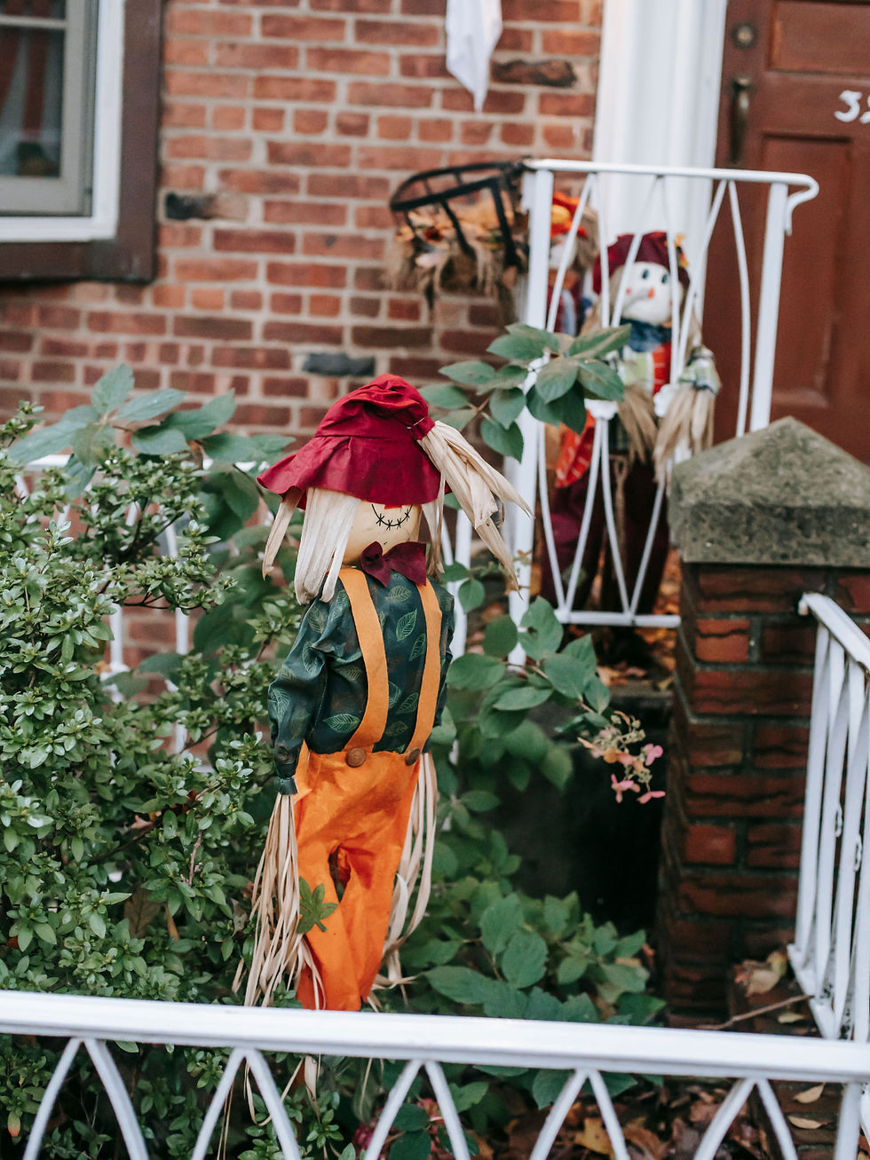Three scarecrow decorations in a brick front yard with white railings and green shrubs, creating a fall scene.