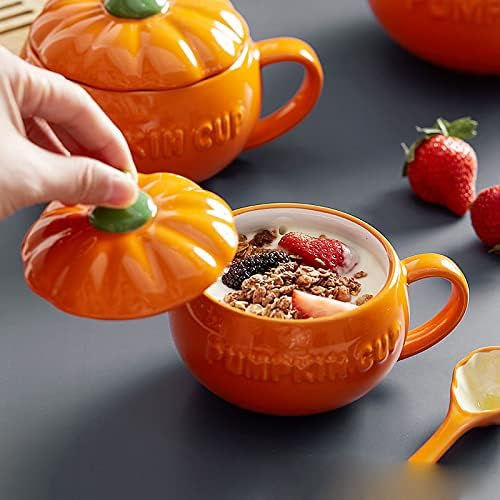 Orange pumpkin-shaped cup with yogurt, granola, and berries. Hand lifts lid. Strawberries and spoon nearby on gray surface. Cozy feel.