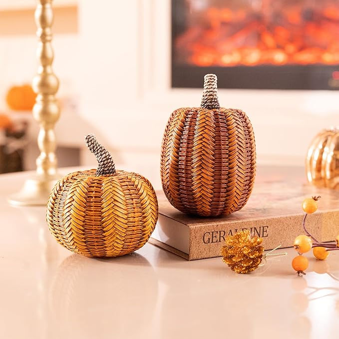 Woven pumpkins on a book labeled Geraldine, with a cozy fireplace in the background. Autumn decor with warm orange tones.