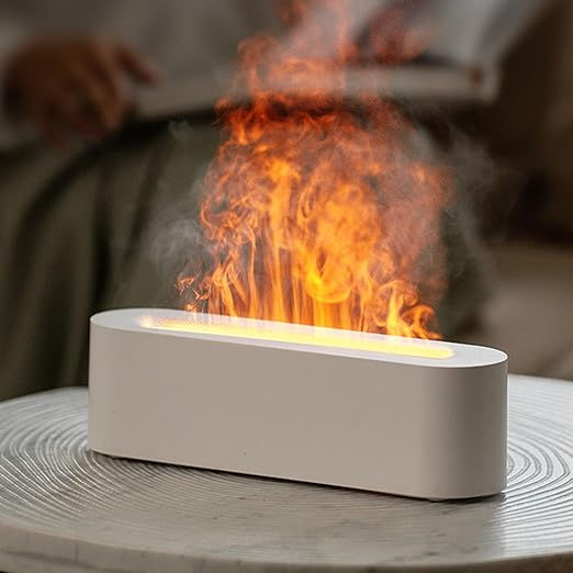 White diffuser emitting orange steam resembling flames, set on a textured table. Blurred figure in background creates a cozy ambiance.