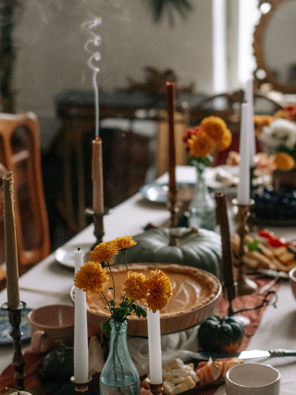 Candles and orange flowers on a cozy autumn table with a pumpkin pie, tea cups, and warm dinnerware in soft candlelight