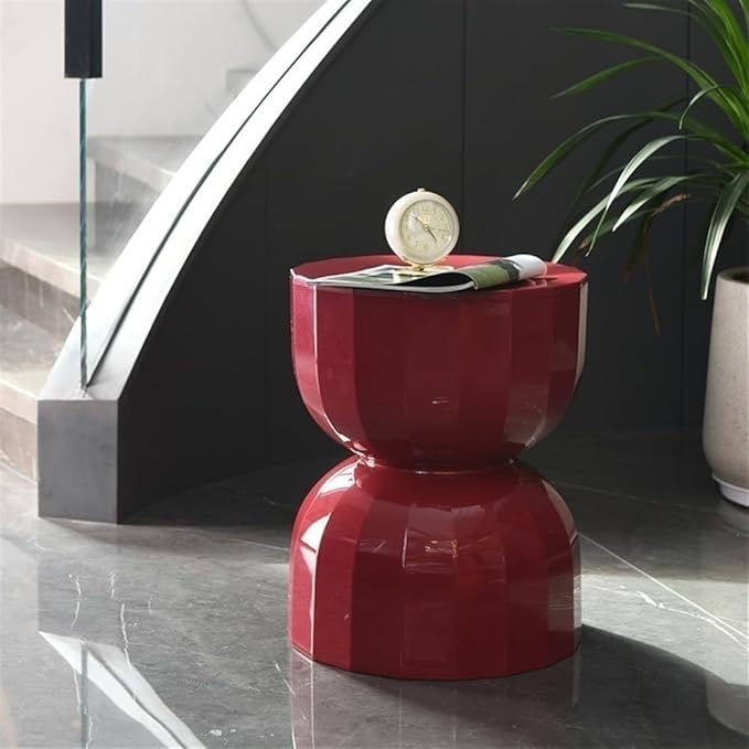 Red stool with a clock and magazine on top, beside a green plant on a shiny marble floor. Modern staircase in the background.
