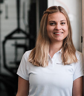 Alisha Zürcher mit weissem Poloshirt lächelt entspannt in die Kamera im Hintergrund erkennt man schwarze Trainingsgeräte