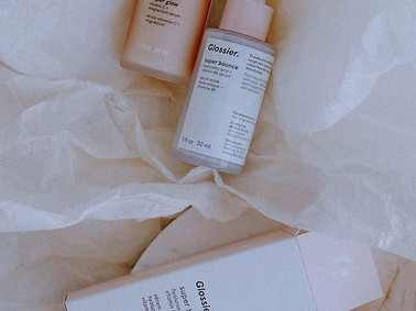 A flatlay image of Glossier skincare bottles laying on cream colored tissue paper