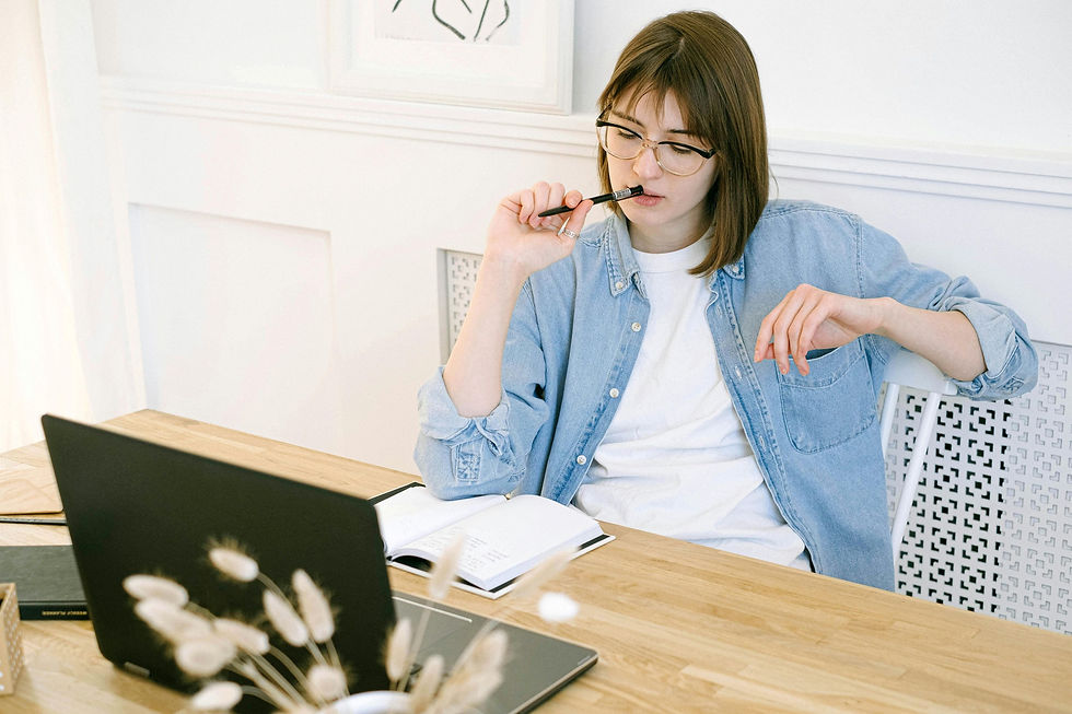 Woman at desk thinking while working on a laptop with a notebook.