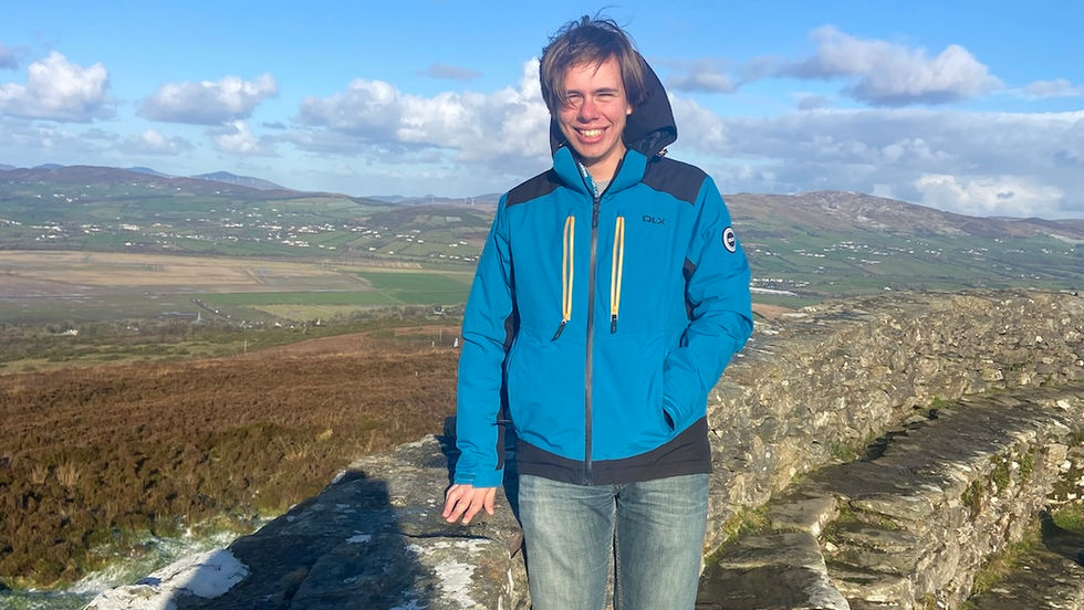 A male student standing on top of a stone hill fort with the Donegal landscape far behind him.