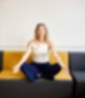 Rebecca Roe sitting on mustard-coloured couch in yoga pose