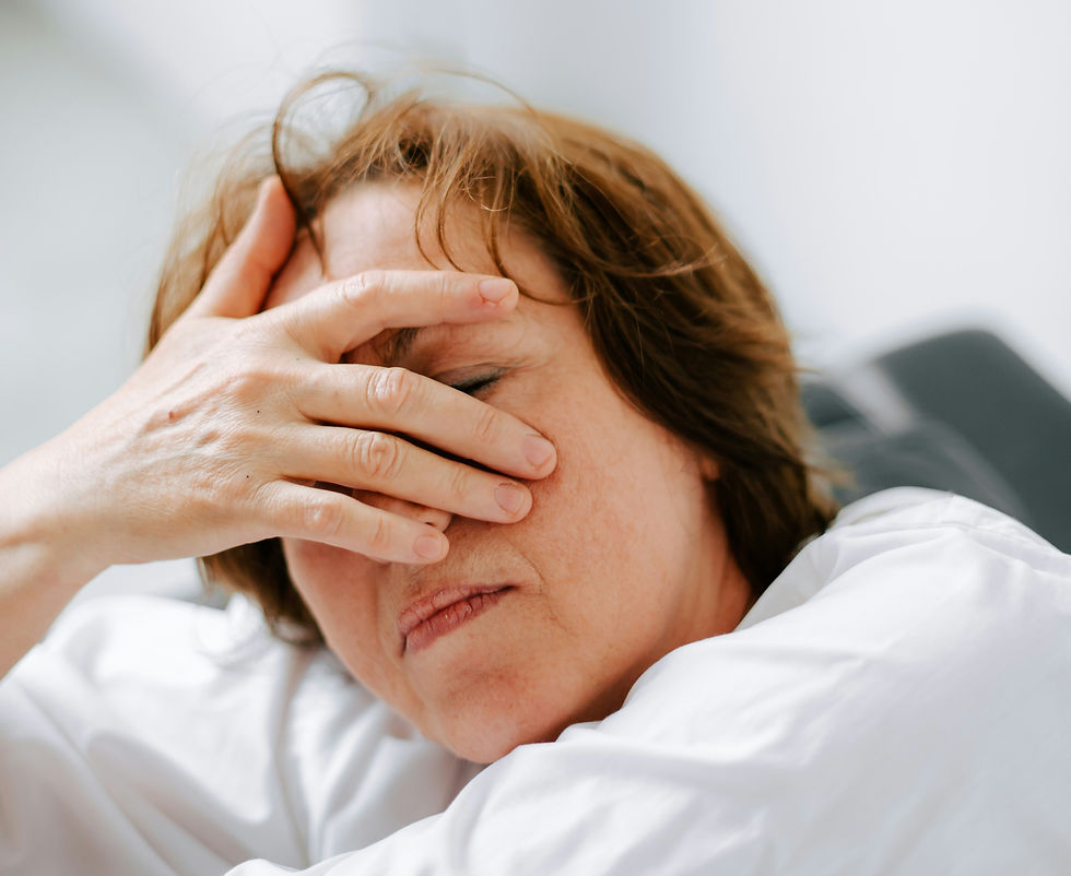 Woman in white shirt covering face with hand, eyes closed, appears stressed. Soft lighting, neutral background sets a contemplative mood.