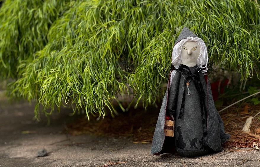 Handmade Witch with broom standing by a green bush