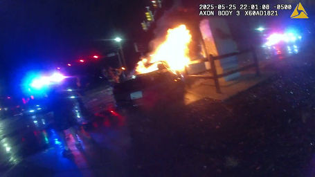 A screenshot of an officer's body camera video showing a burning car on the side of the road.