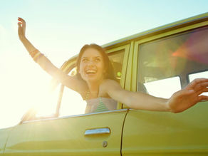 Young woman enjoying a summer road trip with the windows down and sunshine overhead.