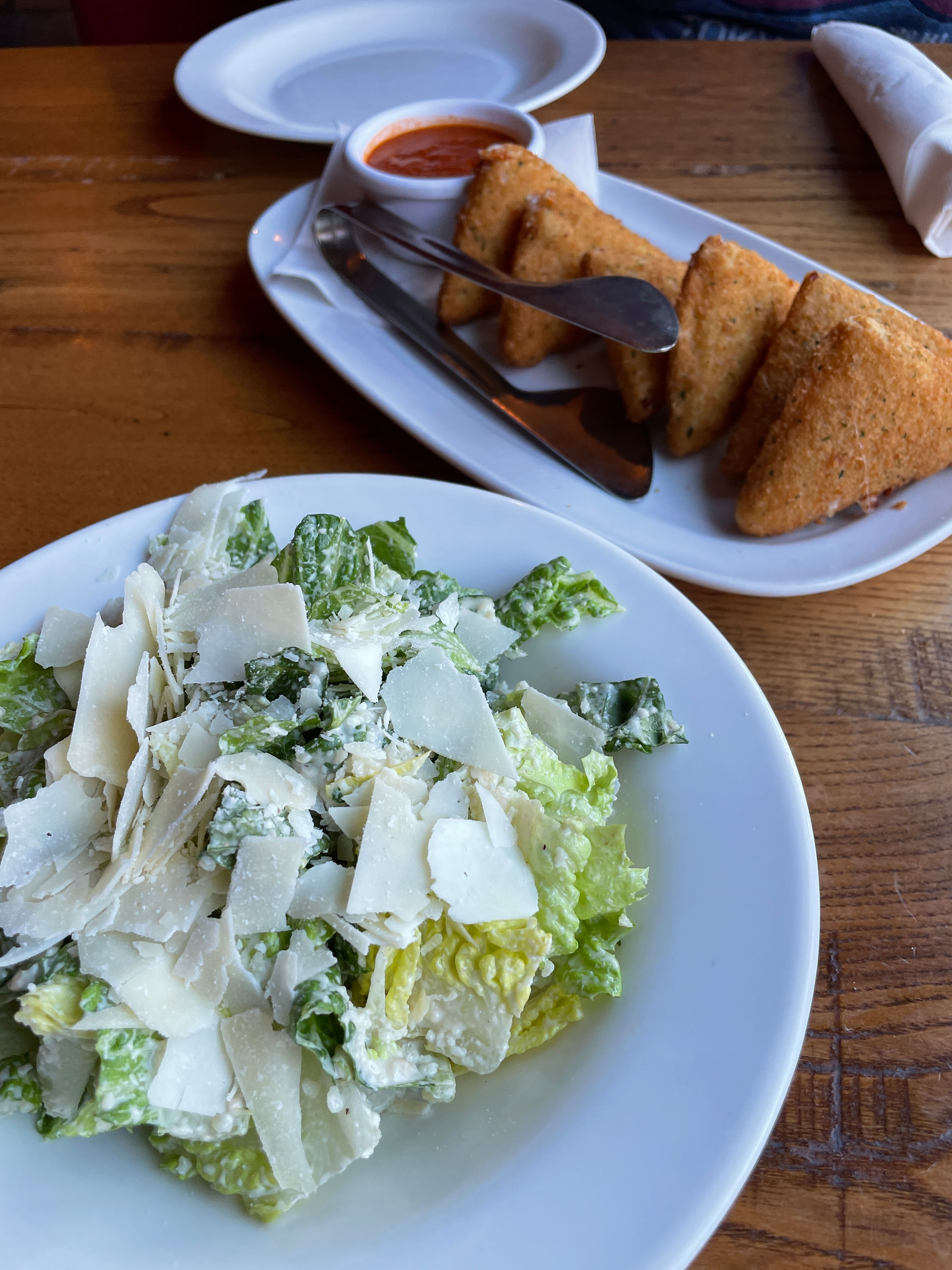 caesar salad with shaved parmesan cheese next to a plate with triangles stuffed with mozzarella cheese