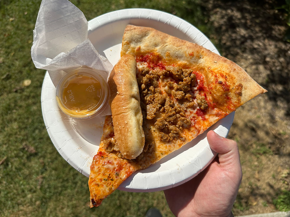 A large, floppy sausage pizza slice on a white paper plate, topped with melted cheese and crumbled sausage, served with a small cup of dipping sauce on the side
