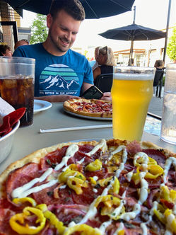 pizza blog smiling while taking photos of pizza beer visible in foreground
