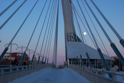 Full moon peeks out from behind the supports of Winnipeg’s Esplanade Louis Riel.