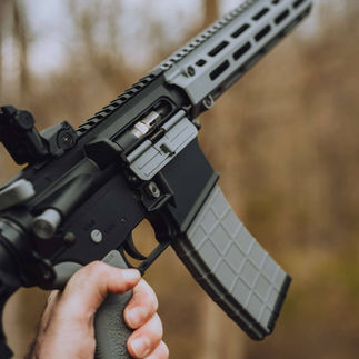 Hand holding a black and gray AR-15 rifle with Tippmann Arms in focus.