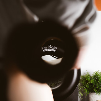 Person holding a black object with "The Boss" visible, near plant and wall.