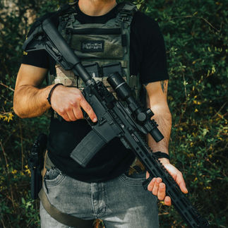 Man in tactical gear holding rifle, Wolfpack Armory, with wooded background