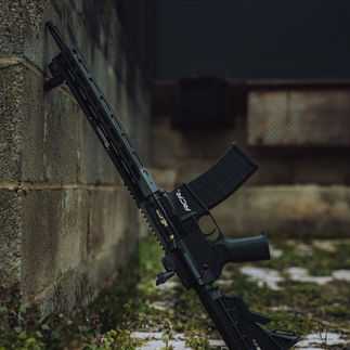 Black rifle leaning against a concrete wall, Tippmann Arms and Mbogo Media.