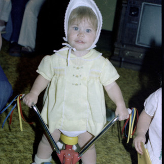 Toddler Mindy Arbuckle sitting on a tricycle in a bonnet, showing early curiosity, innocence, and th