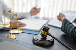 Law office scene with golden scales and a gavel on a desk while two people review and sign documents in bright light
