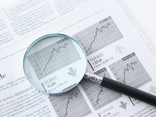 Lupa sobre periódico financiero con gráficos bursátiles y texto de NIKKEI, TOPIX y NASDAQ; tono analítico.