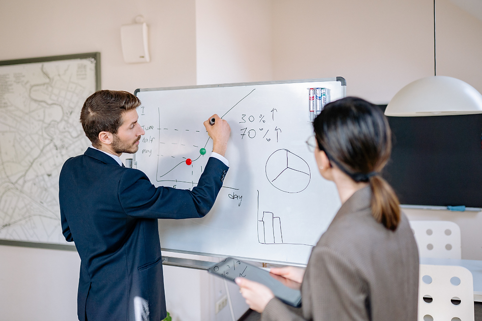 Hombre y mujer en traje observan un gráfico en un pizarrón blanco. Sala luminosa con mapa en la pared. Textos: "30%", "70%". Análisis.