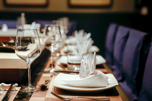Elegant restaurant table set with wine glasses, folded white napkins, and plates beside purple chairs.
