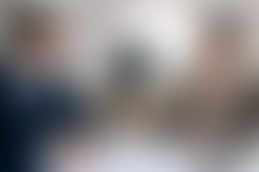 Man in blue suit and woman in glasses review documents at a desk, sharing a smile. Sunlight illuminates the modern office setting.