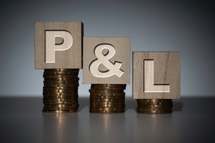 Wooden blocks spelling P&L on stacks of coins against a gray studio background.