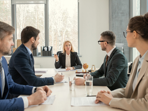 Business team meeting in a bright office, with a woman leading discussion at the head of the table.