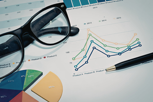 Glasses and a pen rest on a document showing a colorful line graph and pie chart, depicting product data from 2012 to 2015.