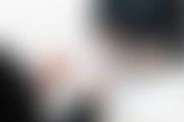 Two people in suits discussing charts and graphs on a table with documents. One holds a tablet. Office setting, light wood surface.