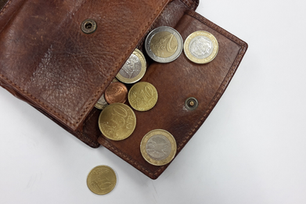 Open brown leather wallet with various Euro coins scattered on a white surface. Coins include 1, 2, 10, and 50-cent pieces.