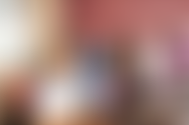 Smiling nurse in blue scrubs holds a file in a therapy room. Behind, therapists assist patients exercising with equipment. Warm, welcoming vibe.