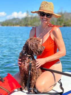 A woman on the water on a paddle board with her wet Australian Labradoodle