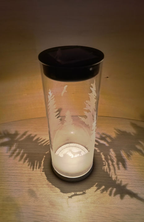 Handgefertigte Solarlampe aus klarem Glas mit mattierter Gravur und Betonfuß, erzeugt sanftes Licht mit Schattenmuster.