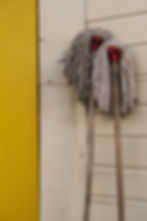 Two dirty string mops with red heads lean against a white wall beside a bright yellow door.