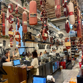 Vista de la isla central del restaurante y los productos distribuidos estilo delicatessen, con salchichas en el techo y una barra amplia de preparados