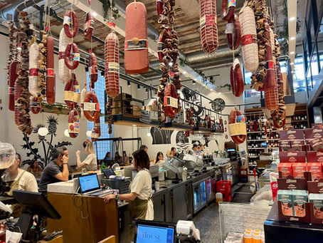 Vista de la isla central del restaurante y los productos distribuidos estilo delicatessen, con salchichas en el techo y una barra amplia de preparados